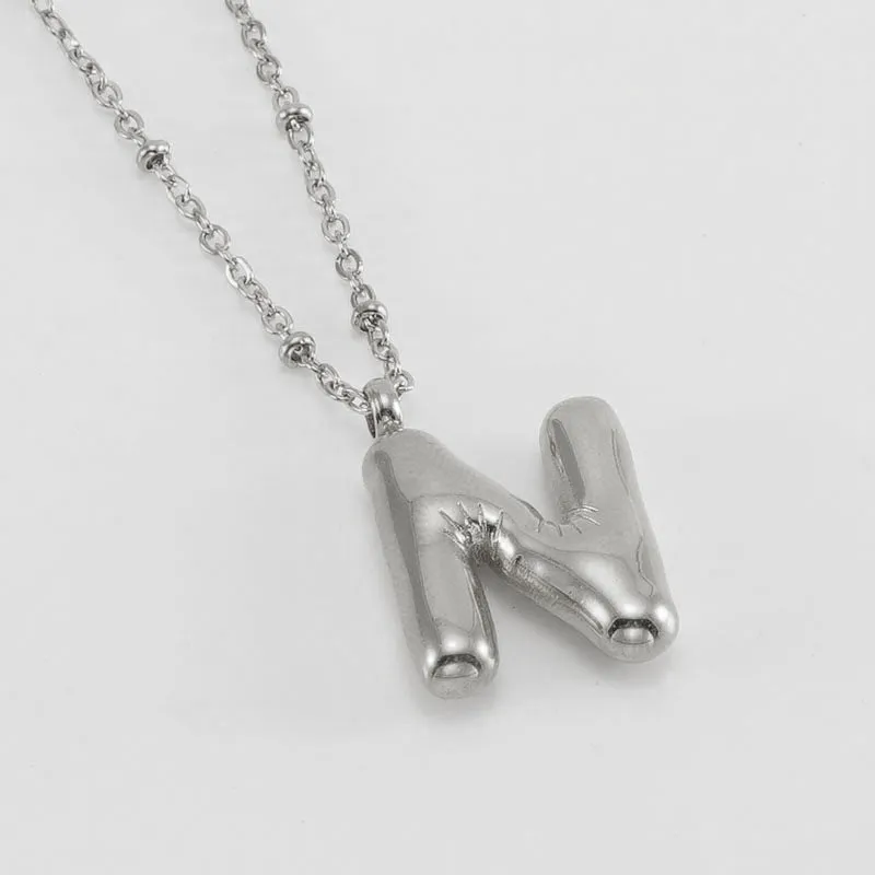 Gold bubble letter N pendant on stainless steel clip beads chain necklace against white background