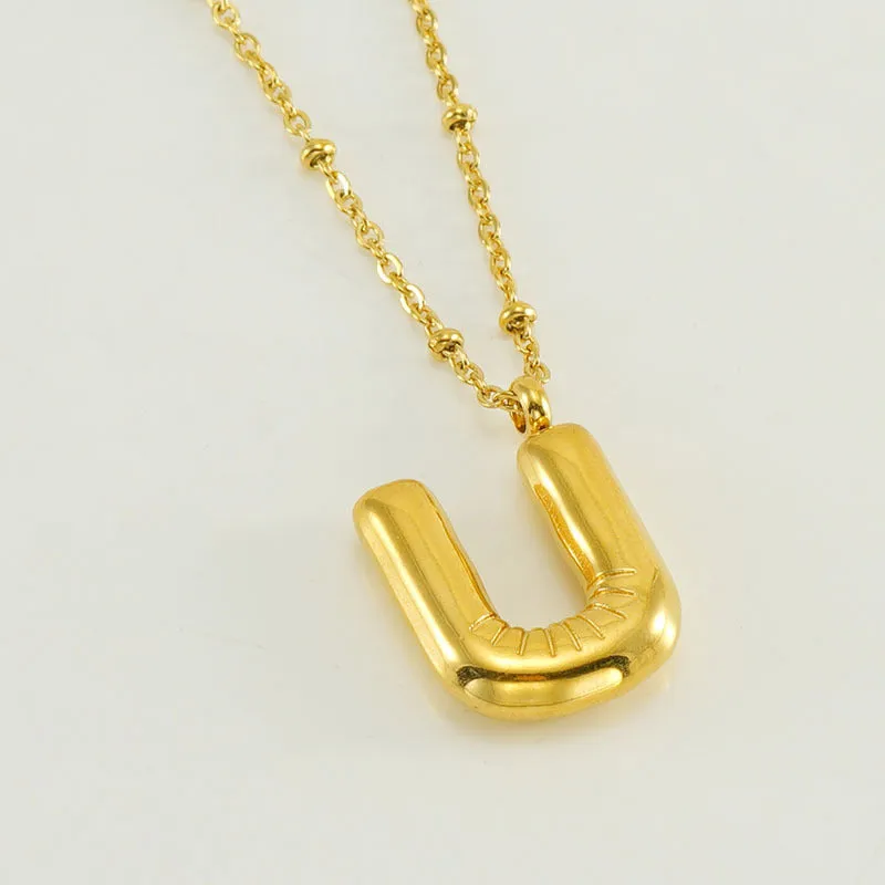Gold bubble letter N pendant on stainless steel clip beads chain necklace against white background