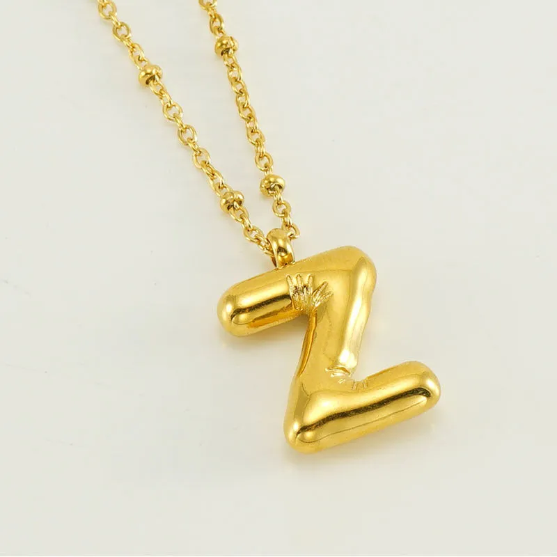 Gold bubble letter N pendant on stainless steel clip beads chain necklace against white background