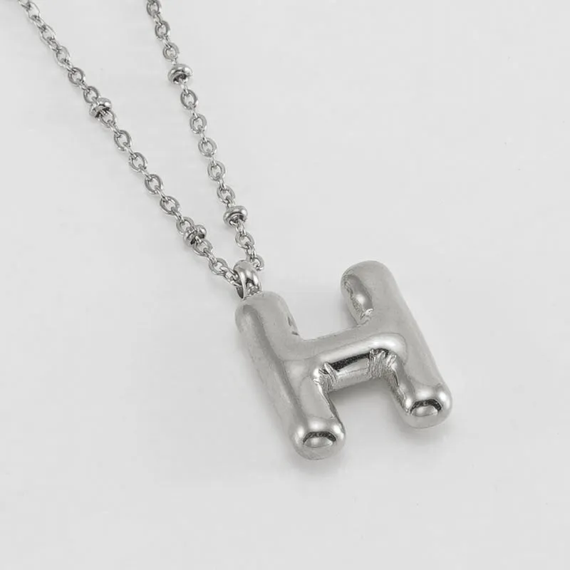 Gold bubble letter N pendant on stainless steel clip beads chain necklace against white background