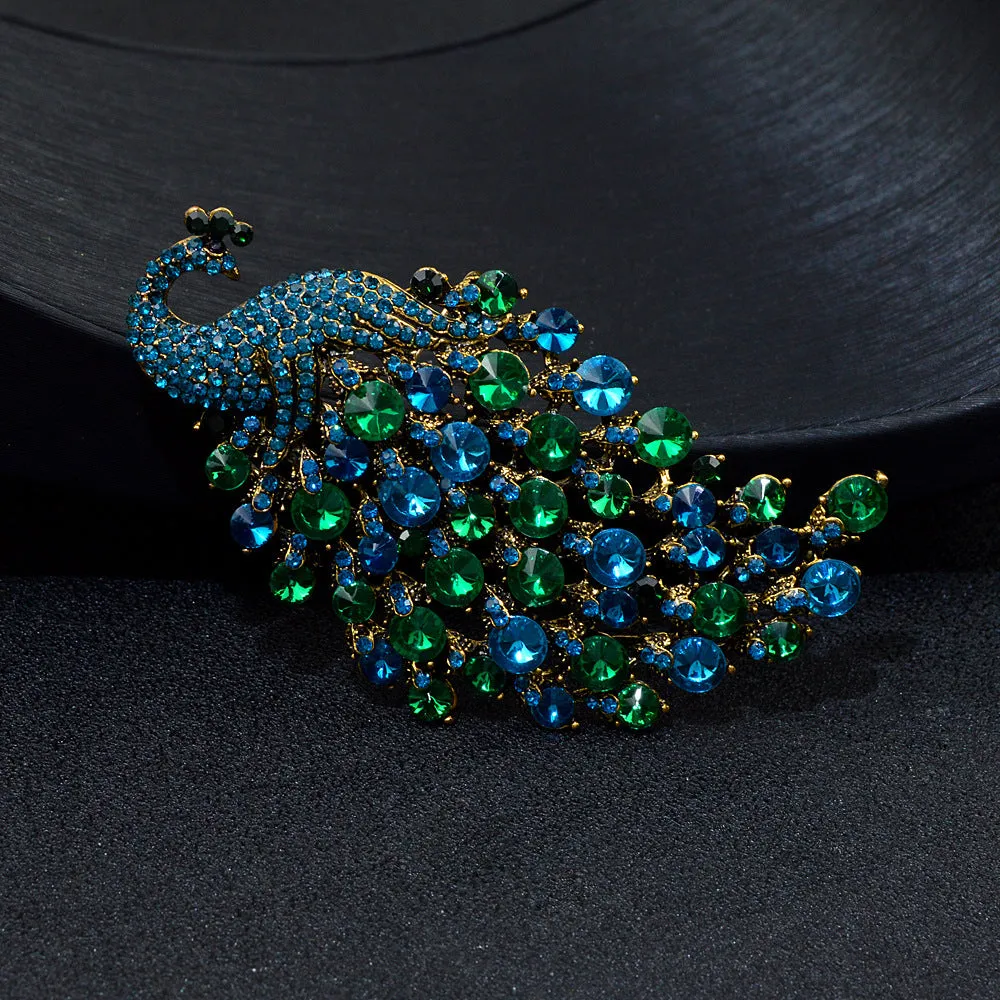 Colourful metal peacock brooch in red, green, and blue with rhinestone accents on a white background