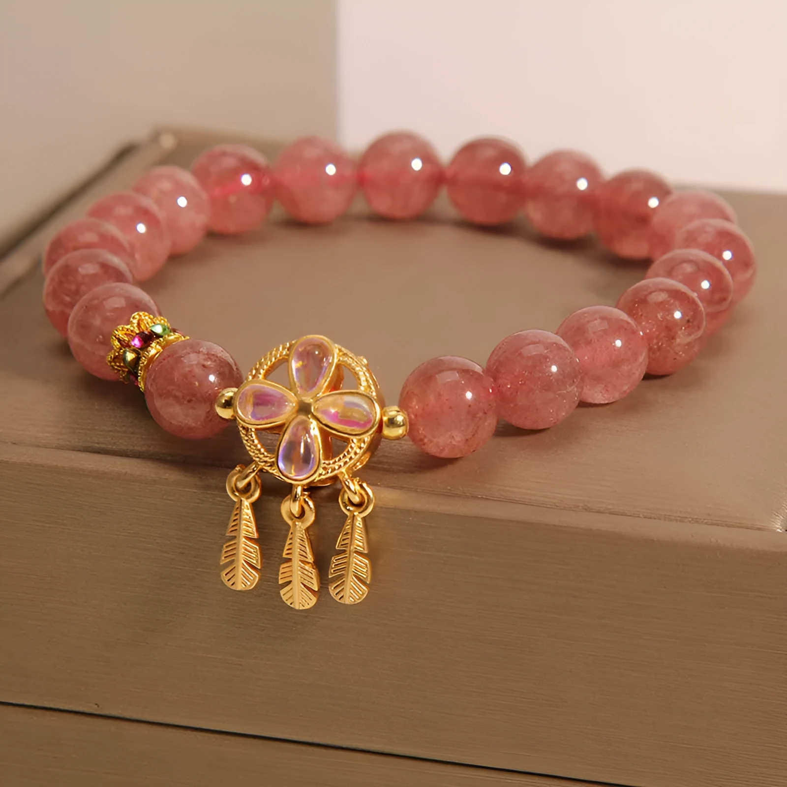 Women's strawberry quartz dream catcher ball pendant bracelet on wrist.
