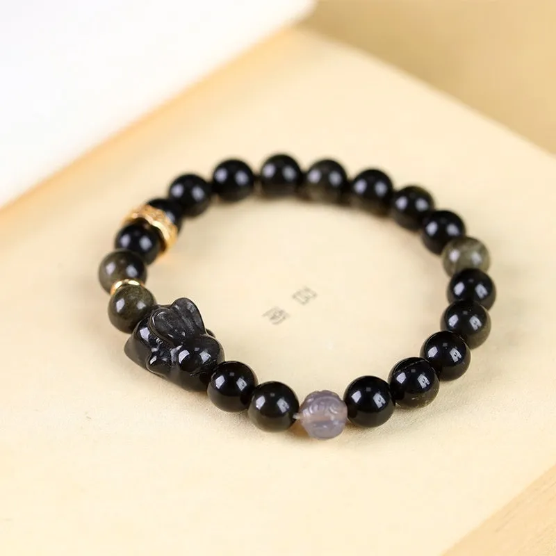 Handmade grey obsidian lying rabbit bracelet with brass and silver details on a wrist, shown in 8mm and 10mm size options.
