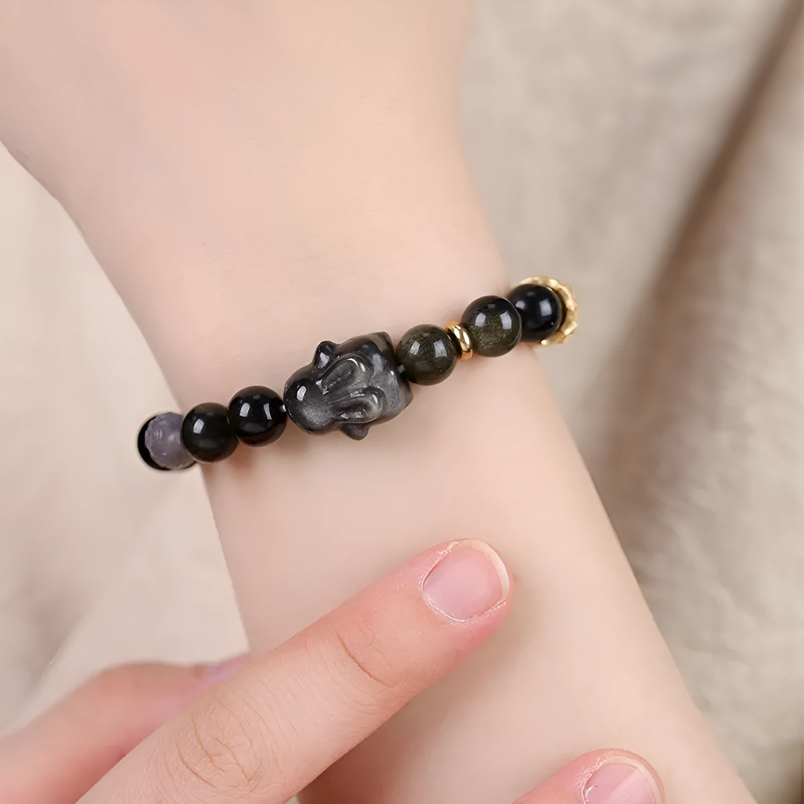 Handmade grey obsidian lying rabbit bracelet with brass and silver details on a wrist, shown in 8mm and 10mm size options.