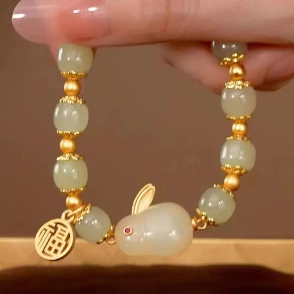 Green jade hare bracelet on wrist showing fu character and lily design details.