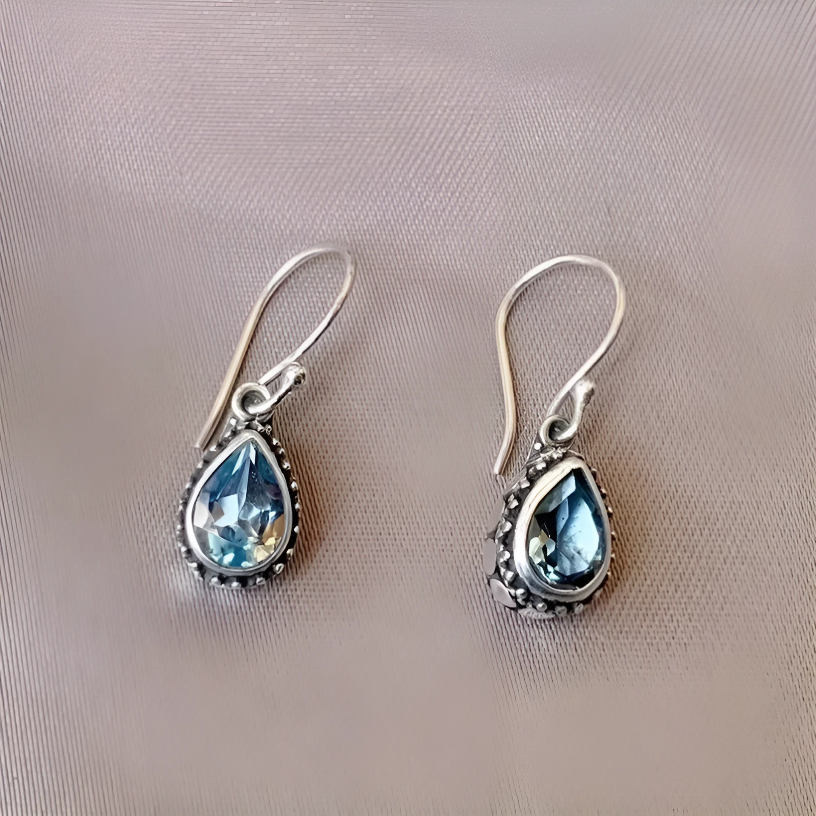 Pair of retro drop-shaped silver alloy earrings with blue gem inlay on white background