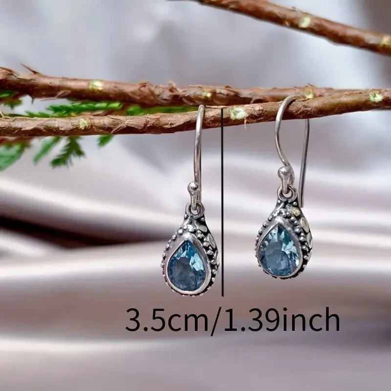 Pair of retro drop-shaped silver alloy earrings with blue gem inlay on white background