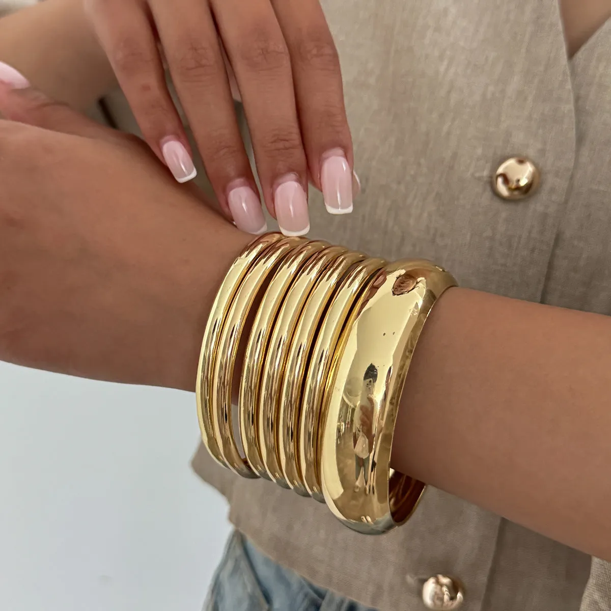 Exaggerated wide round glossy metal bracelet in gold tone on plain background