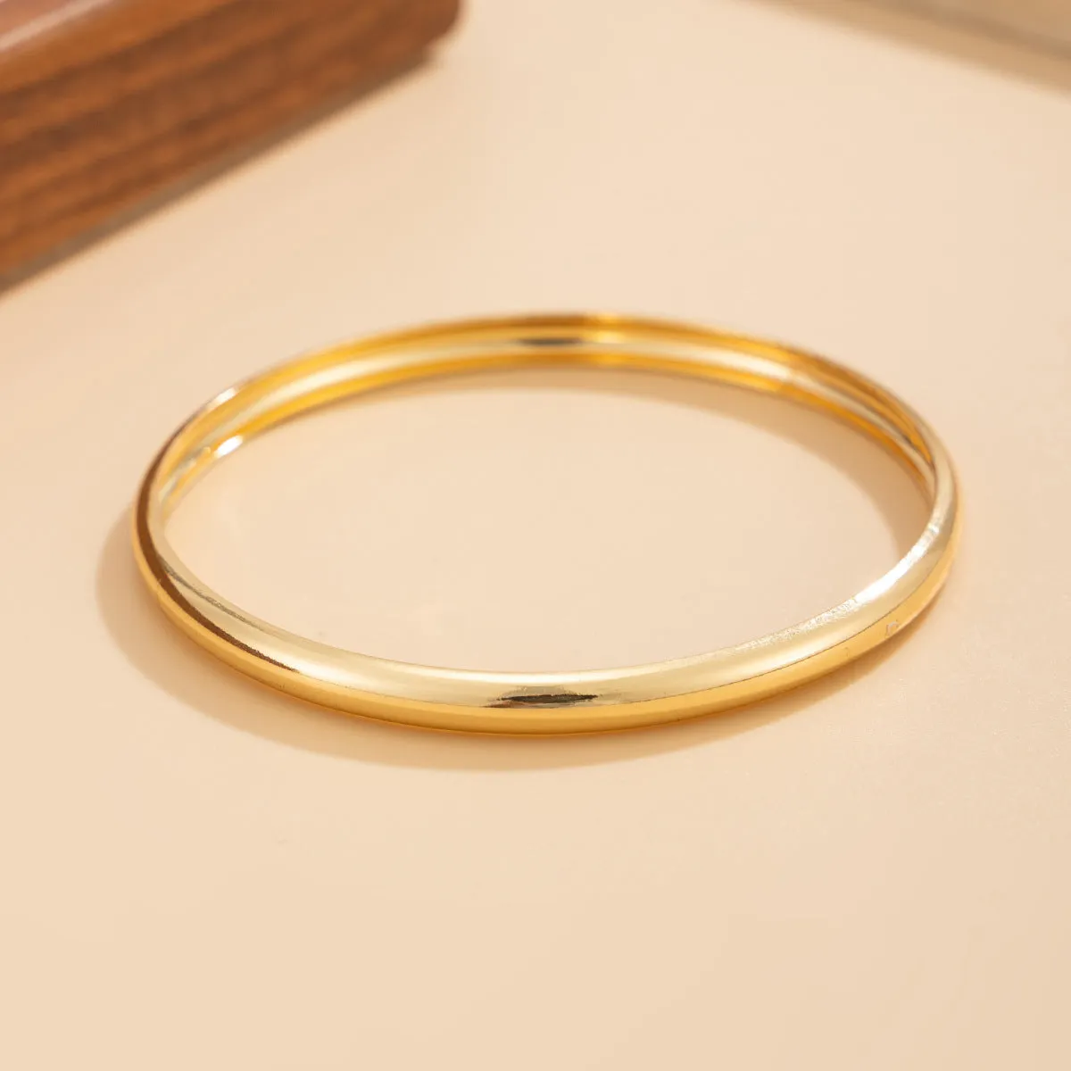 Exaggerated wide round glossy metal bracelet in gold tone on plain background