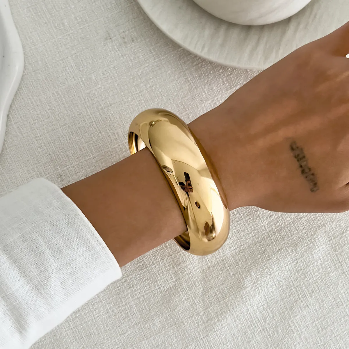 Exaggerated wide round glossy metal bracelet in gold tone on plain background