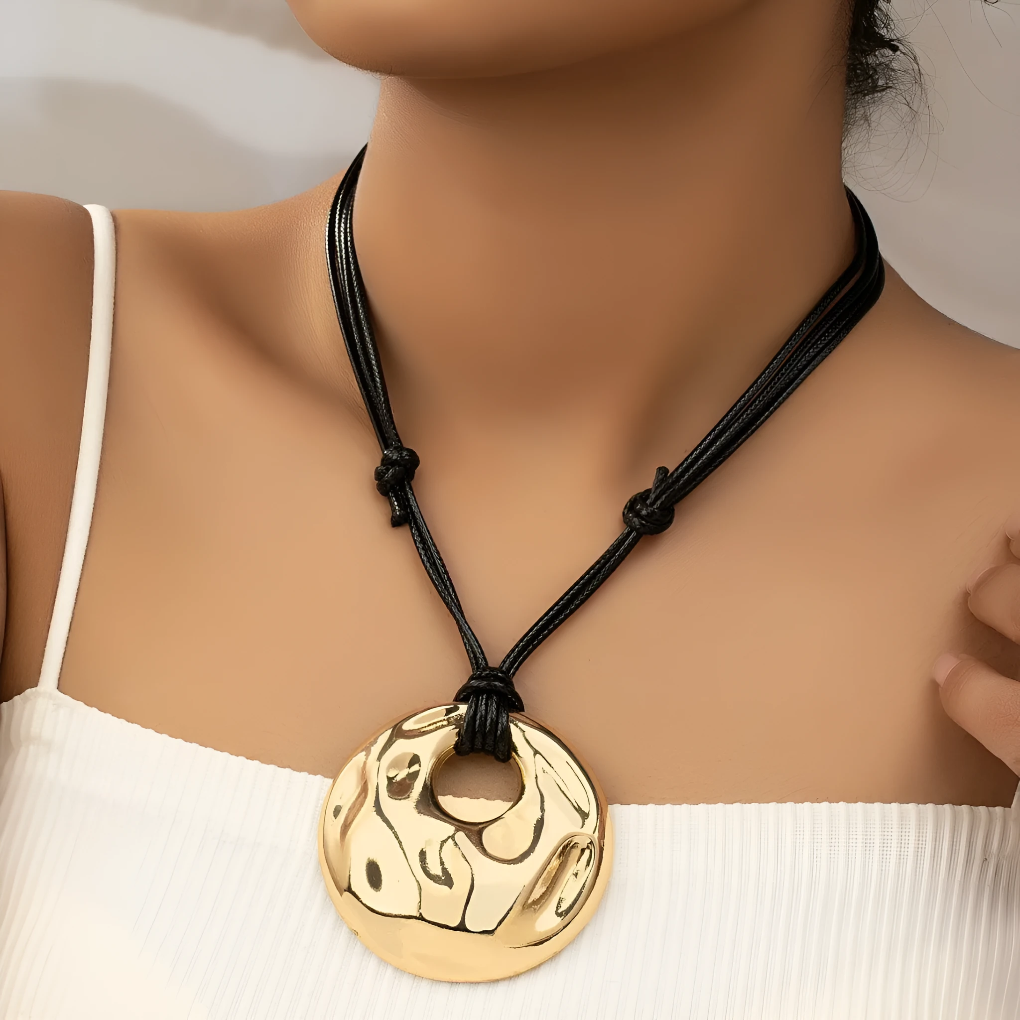 Women's gold alloy oval pendant necklace with braided rope chain on a plain background