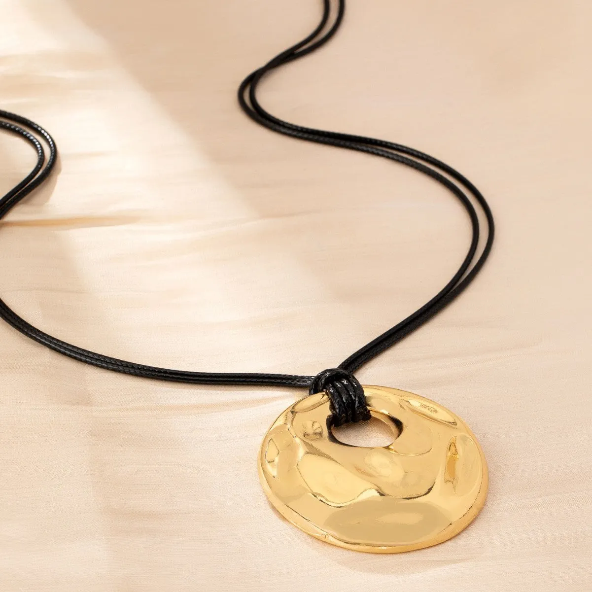 Women's gold alloy oval pendant necklace with braided rope chain on a plain background