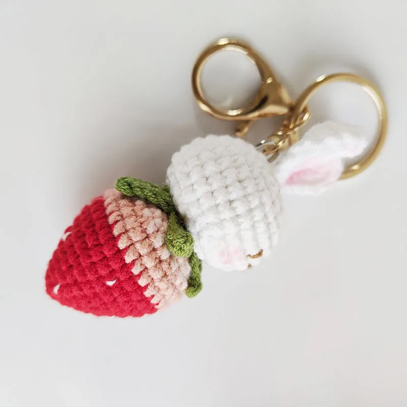 Close-up of a white hand-woven wire rabbit keychain pendant with a strawberry pattern detail.