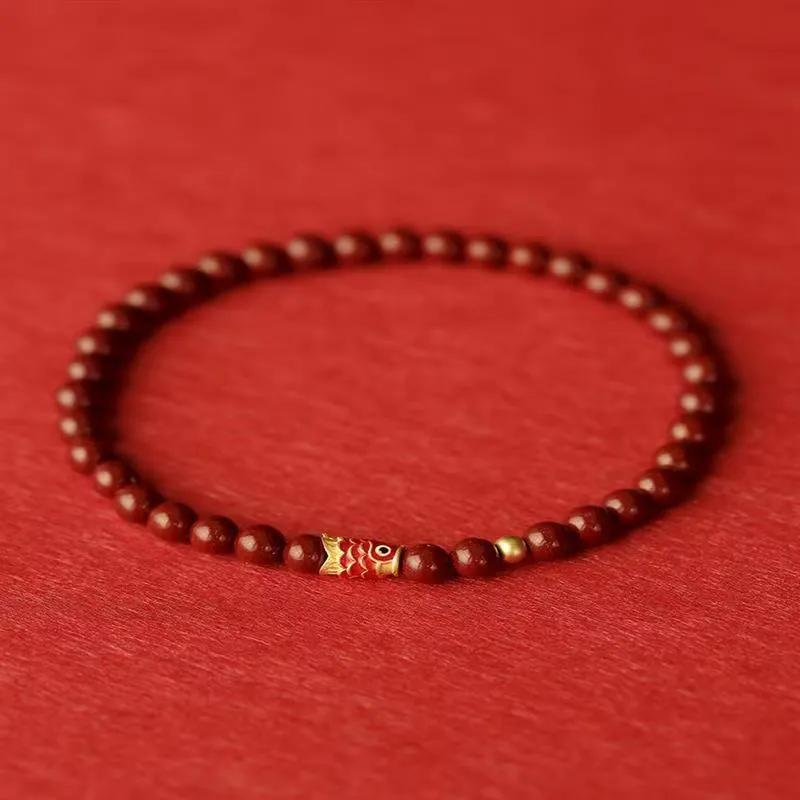 Handmade natural cinnabar koi bracelet with gold balls on a bead, showing traditional Chinese style.