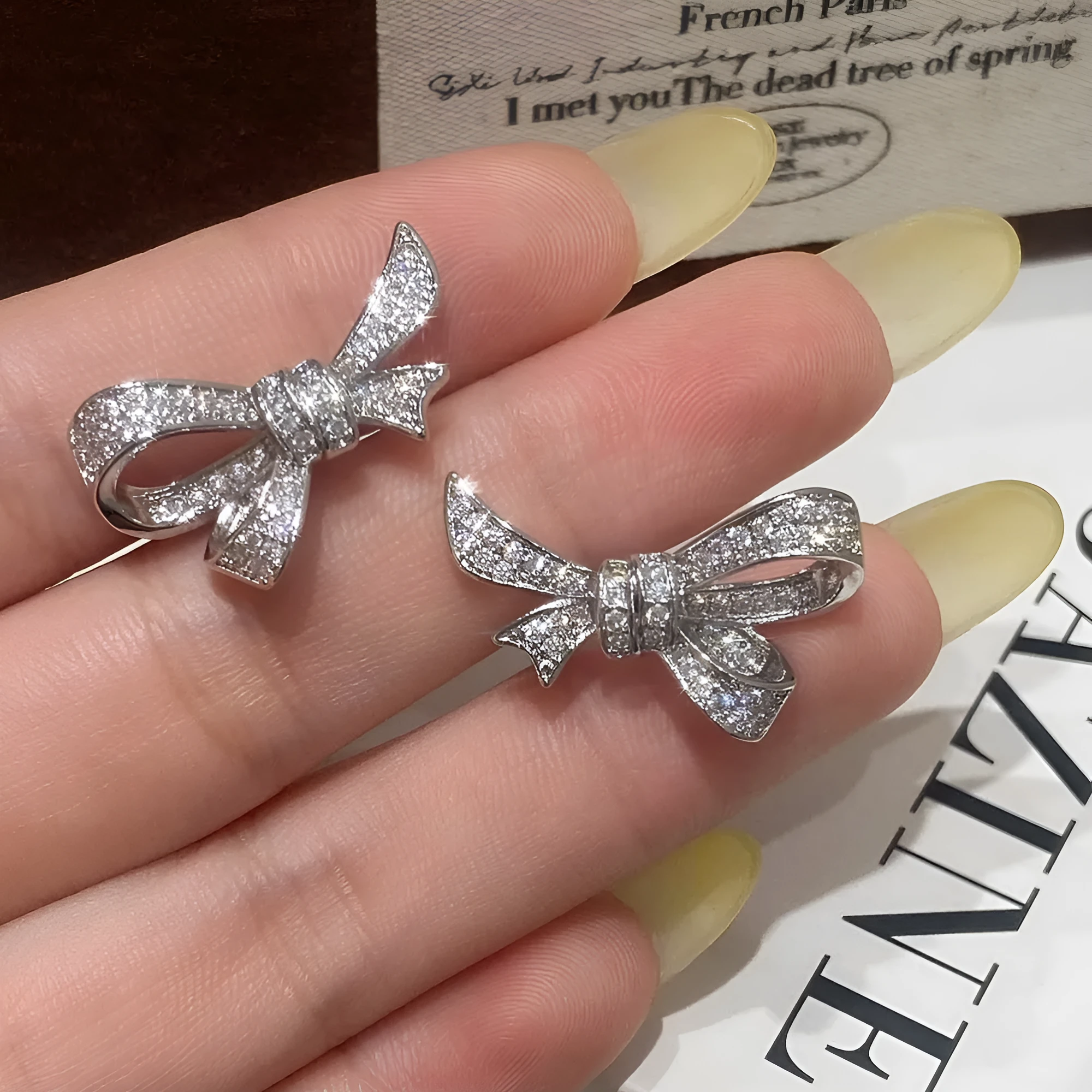 Gold electroplated bowknot ear studs with miniature zircon inlay and 925 silver needle on white background