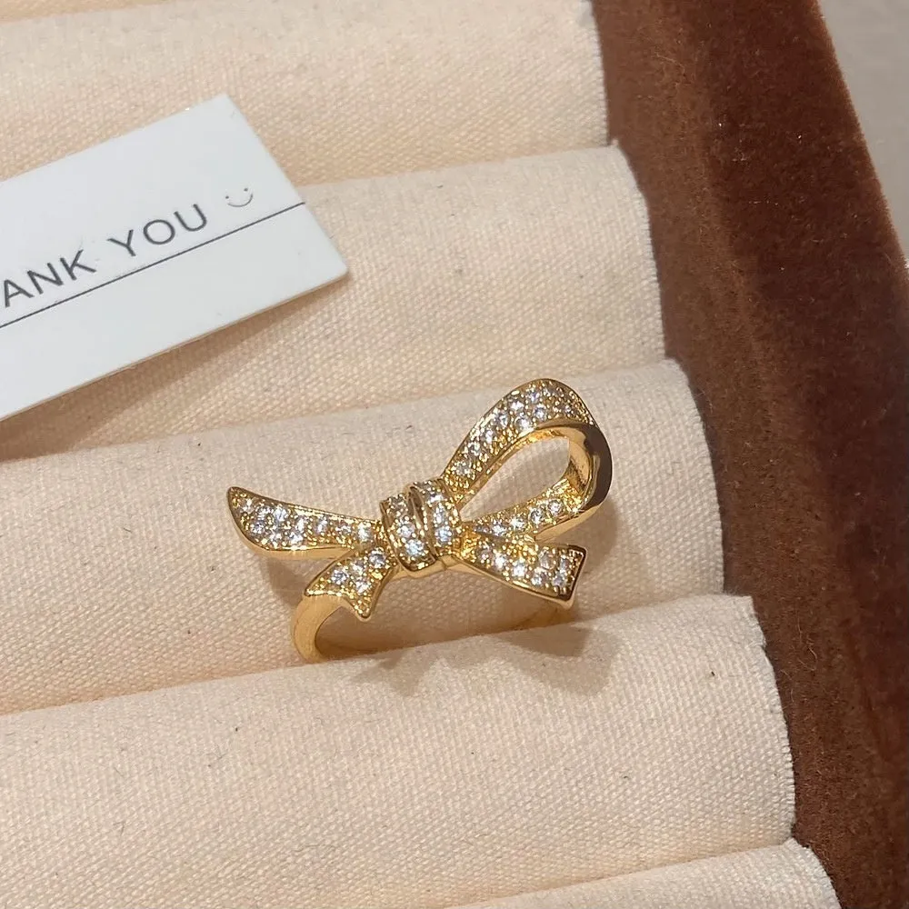 Gold electroplated bowknot ear studs with miniature zircon inlay and 925 silver needle on white background