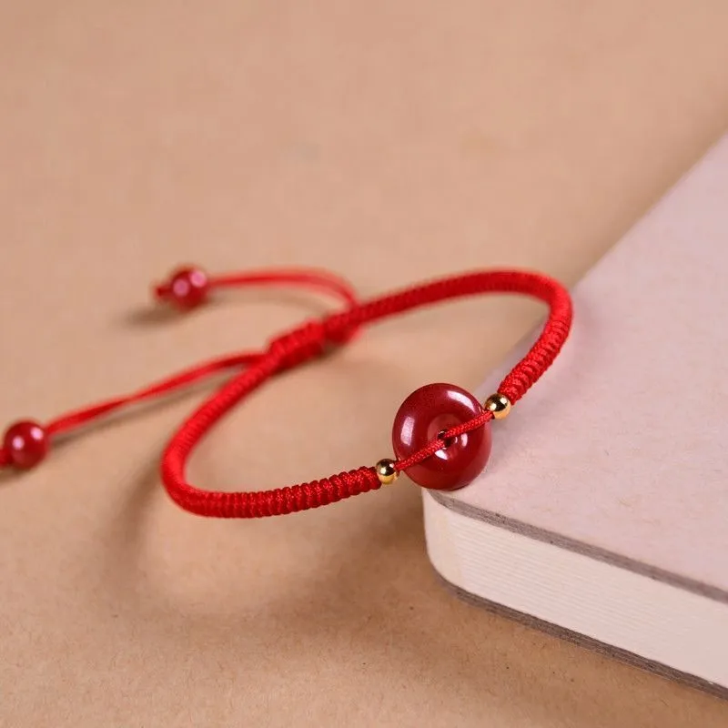 Traditional cinnabar bracelet with a heart-shaped peace buckle clasp on a red rope.