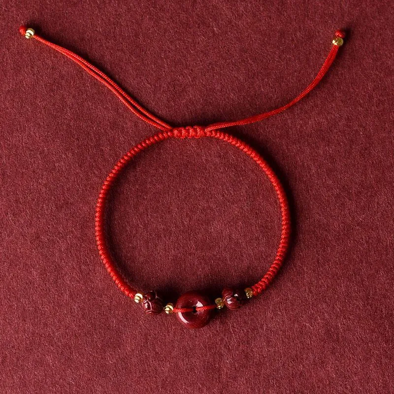 Traditional cinnabar bracelet with a heart-shaped peace buckle clasp on a red rope.