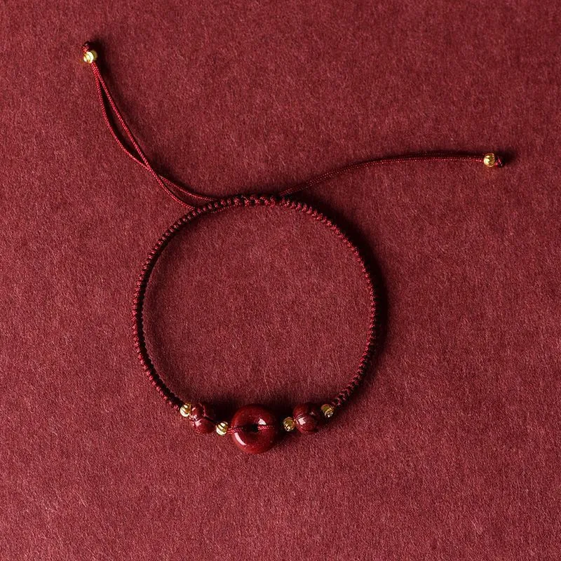 Traditional cinnabar bracelet with a heart-shaped peace buckle clasp on a red rope.