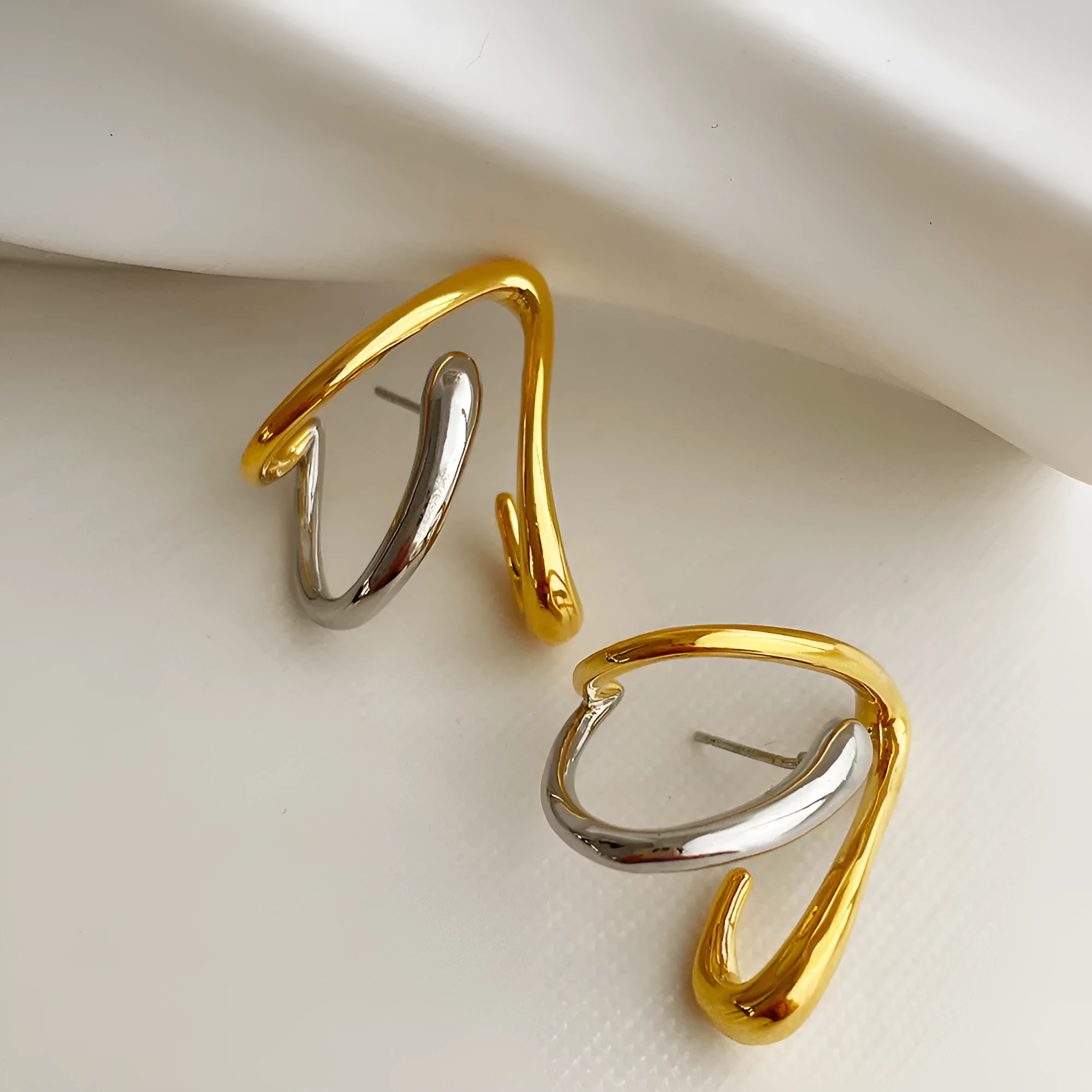 Gold and silver irregular triangle alloy stud earrings with sterling silver needle on neutral background