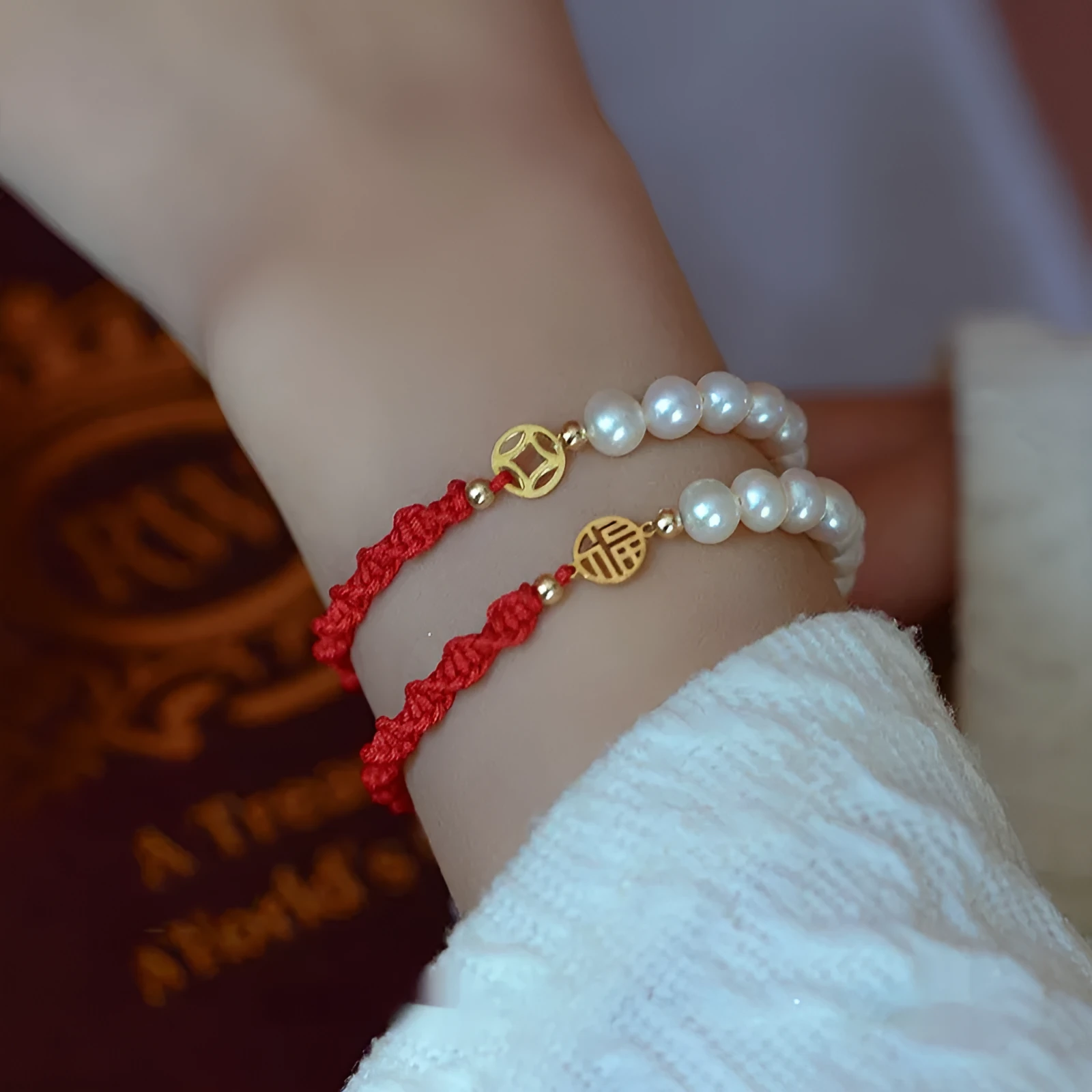 Close-up of a women's pearl and braided red rope bracelet with a gold-plated geometric fu character charm.