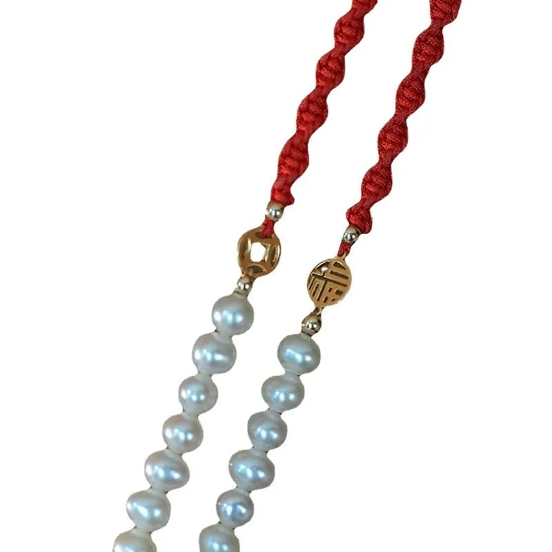 Close-up of a women's pearl and braided red rope bracelet with a gold-plated geometric fu character charm.