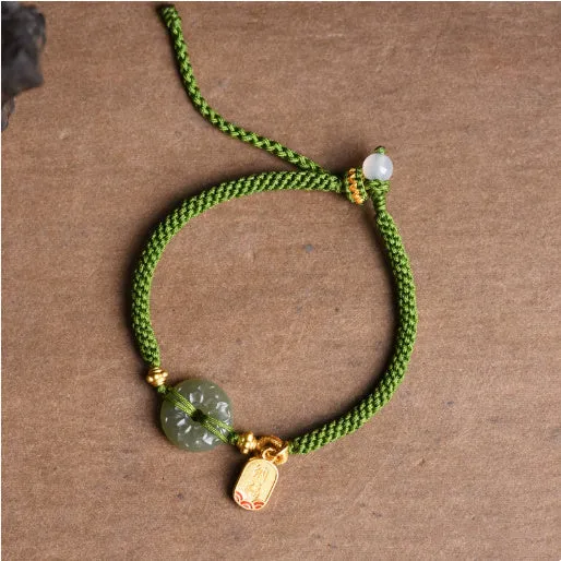 Close-up of a women's hand-woven green rope bracelet with a Hetian jade peace buckle charm.