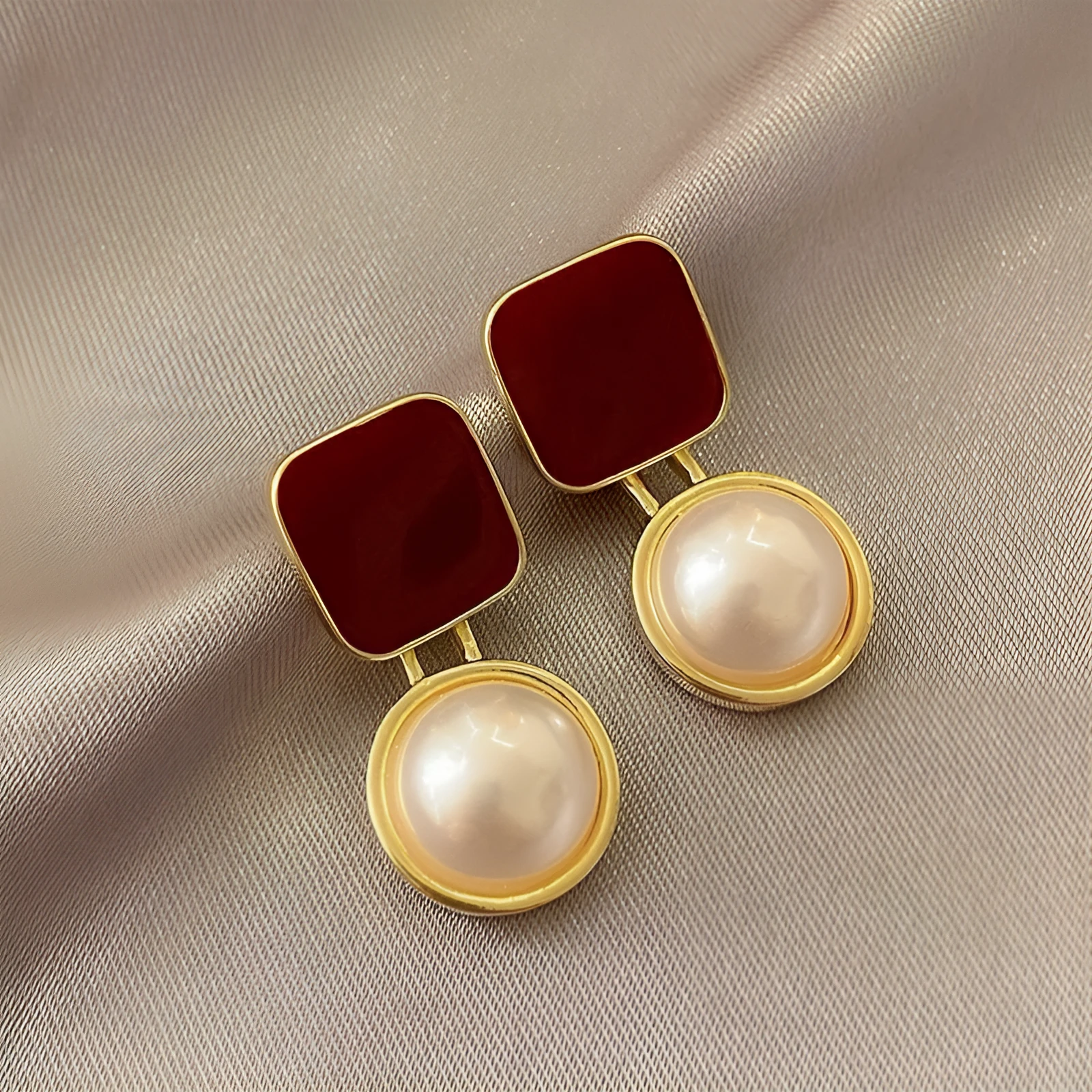 Red and blue geometric alloy stud earrings with pearl centre on neutral background