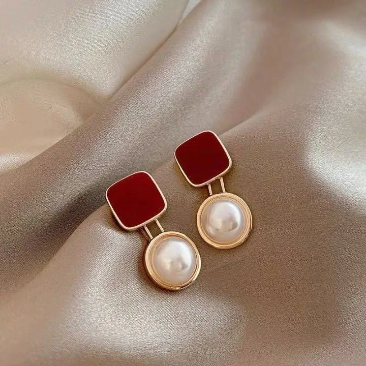 Red and blue geometric alloy stud earrings with pearl centre on neutral background