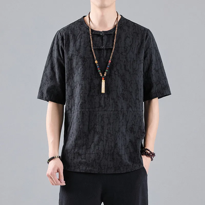 Man wearing a black loose-fit linen t-shirt with a retro jacquard pattern and fastener decoration.