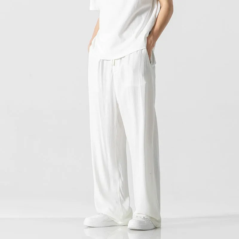 Men's beige loose straight-leg linen trousers with a drawstring waist, shown in a casual summer setting.