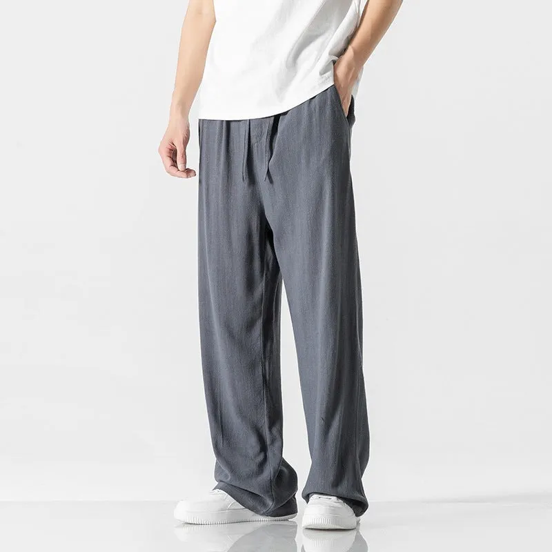 Men's beige loose straight-leg linen trousers with a drawstring waist, shown in a casual summer setting.