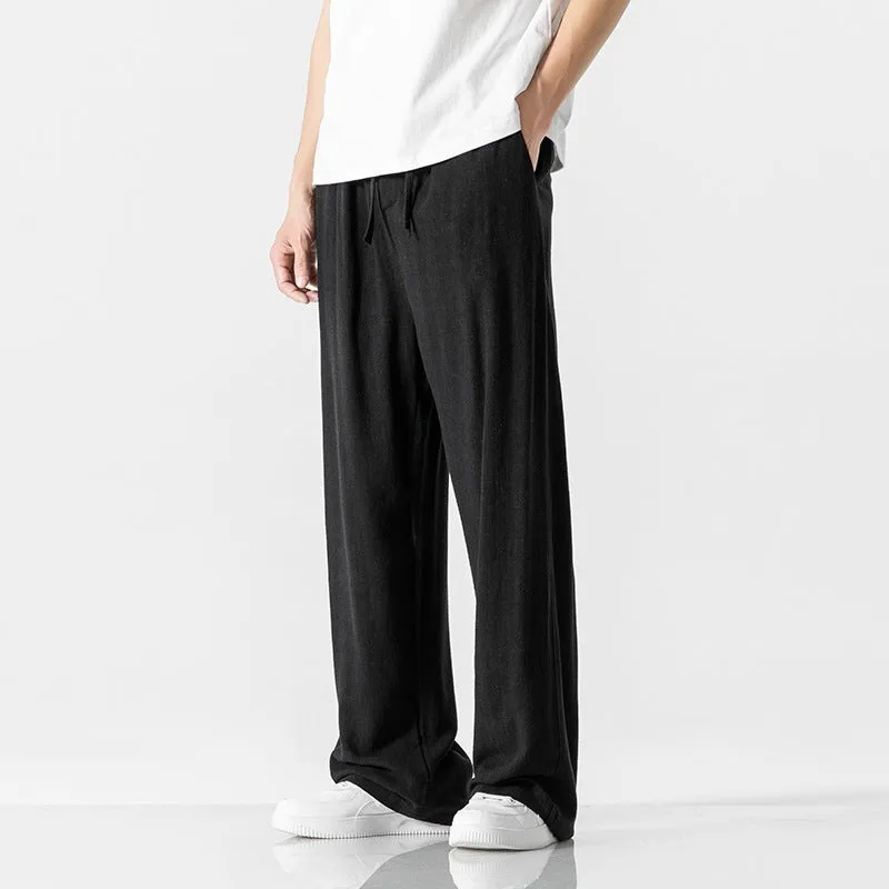 Men's beige loose straight-leg linen trousers with a drawstring waist, shown in a casual summer setting.