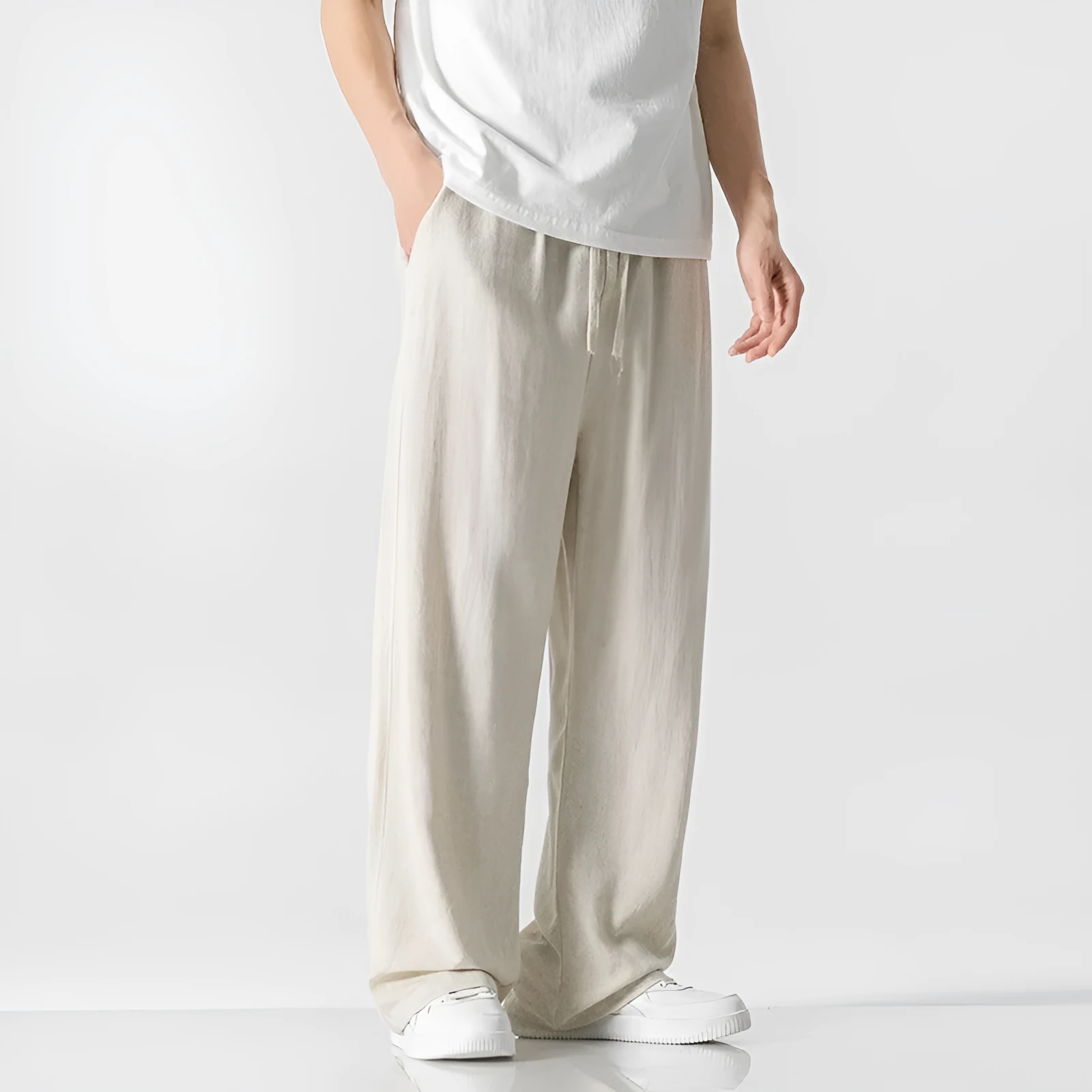 Men's beige loose straight-leg linen trousers with a drawstring waist, shown in a casual summer setting.