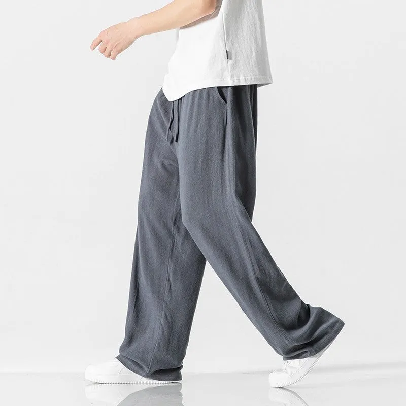 Men's beige loose straight-leg linen trousers with a drawstring waist, shown in a casual summer setting.