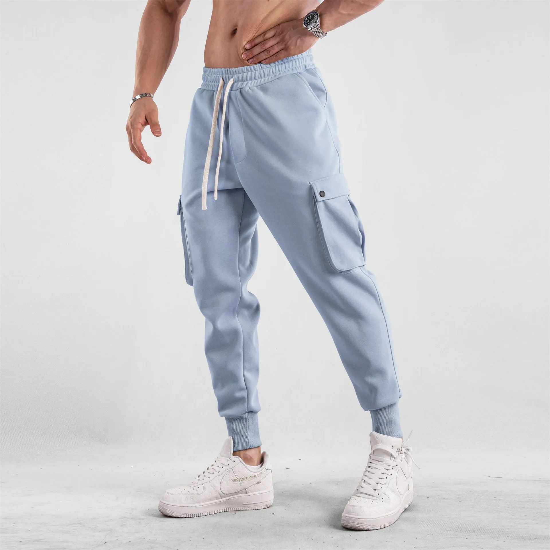 Men's loose light grey cotton trousers with ankle ties and multiple pockets laid flat.