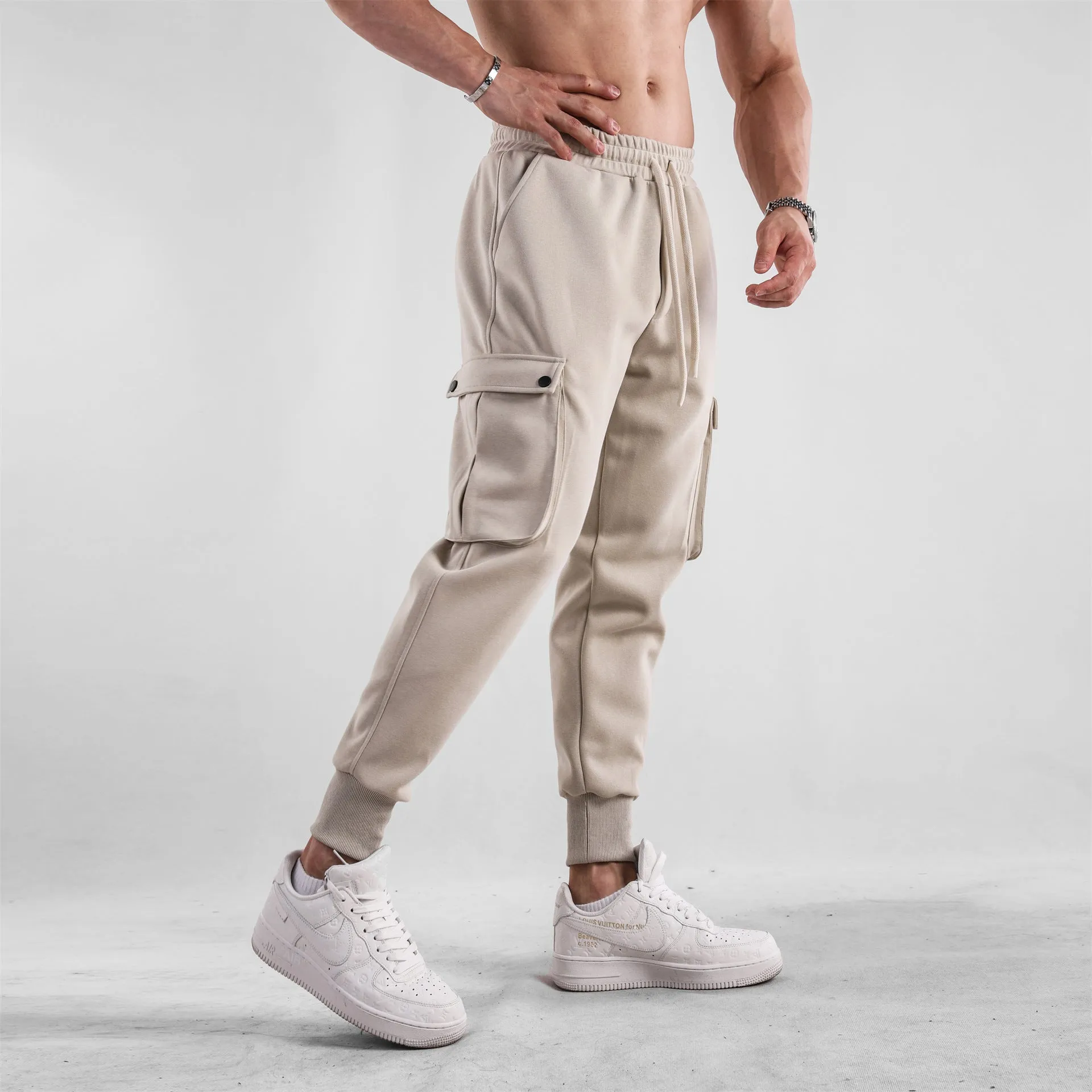 Men's loose light grey cotton trousers with ankle ties and multiple pockets laid flat.