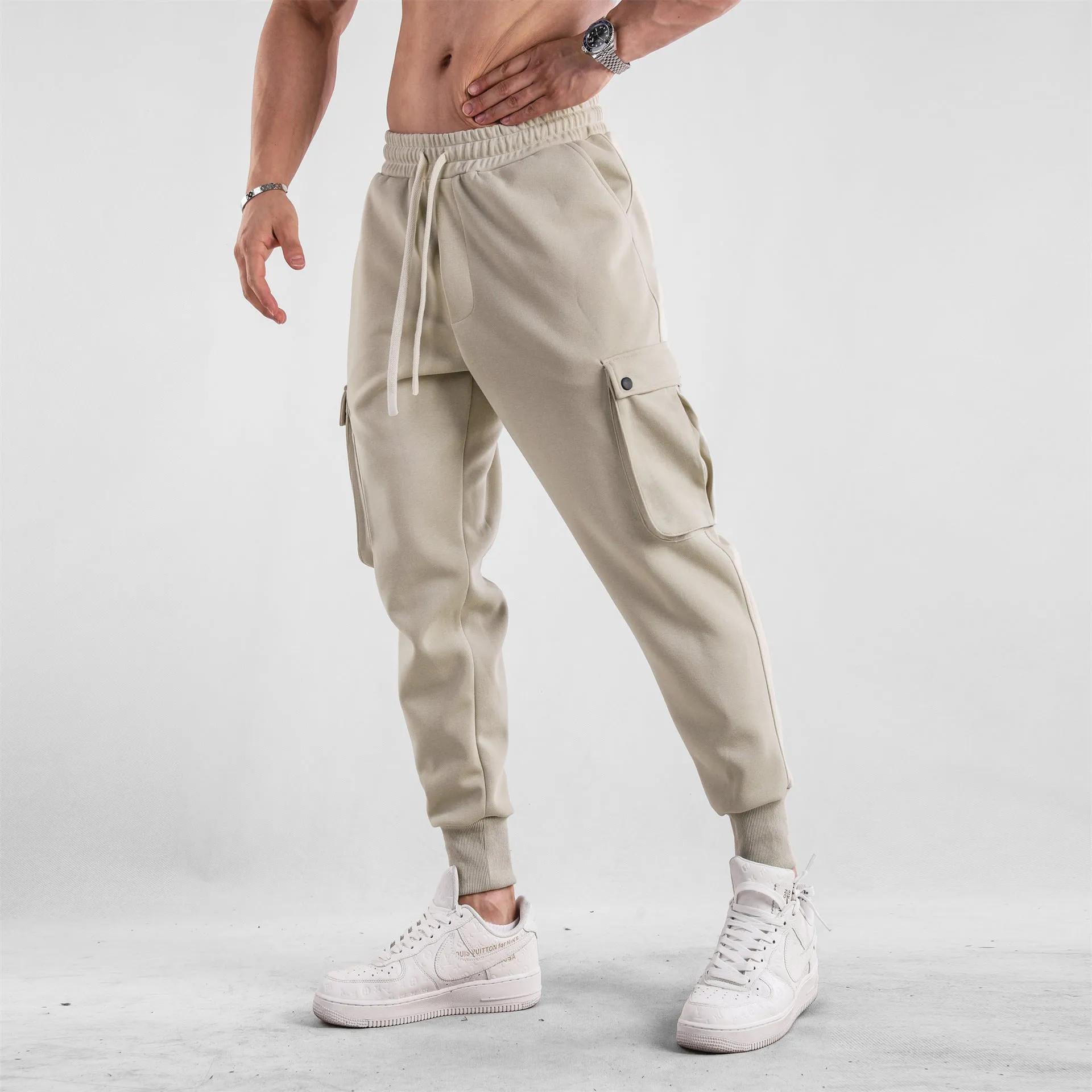 Men's loose light grey cotton trousers with ankle ties and multiple pockets laid flat.
