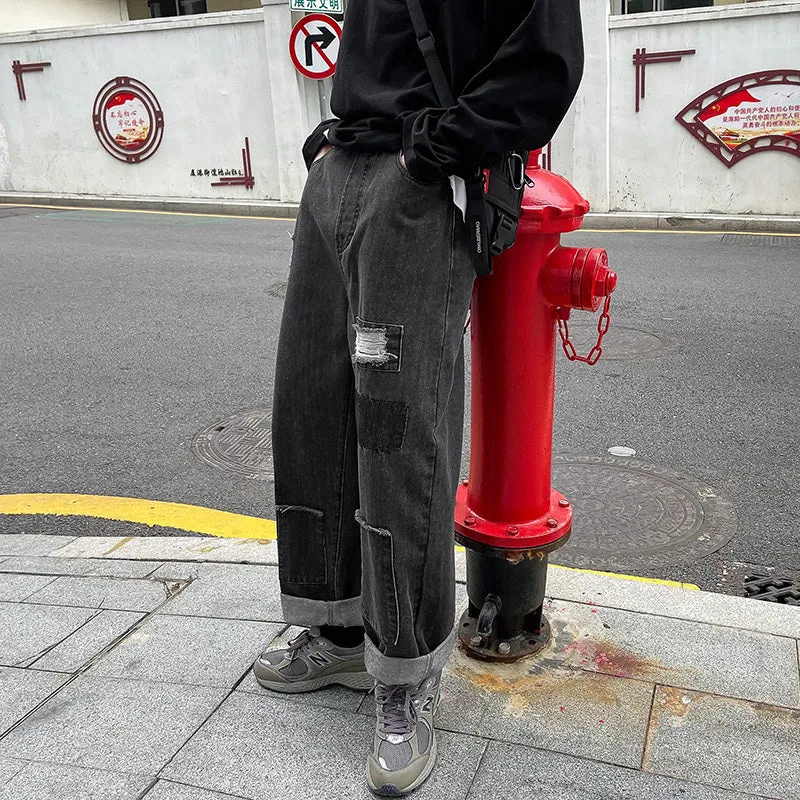 Men's high street ripped jeans with loose straight leg fit in black, showing rips on front thigh area