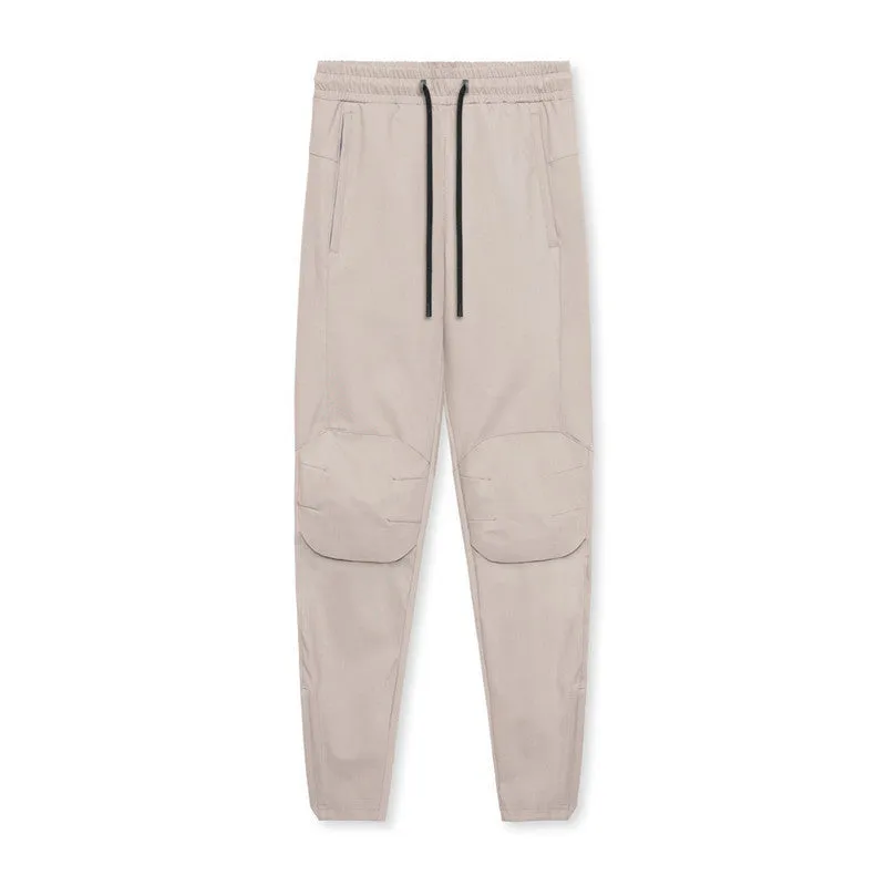 Man wearing loose grey running trousers with tied ankles, made from quick-dry polyester fabric.