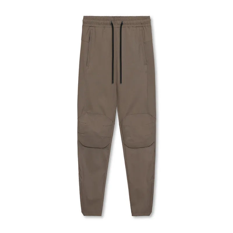 Man wearing loose grey running trousers with tied ankles, made from quick-dry polyester fabric.