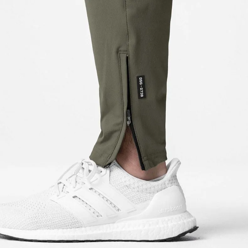 Man wearing loose grey running trousers with tied ankles, made from quick-dry polyester fabric.