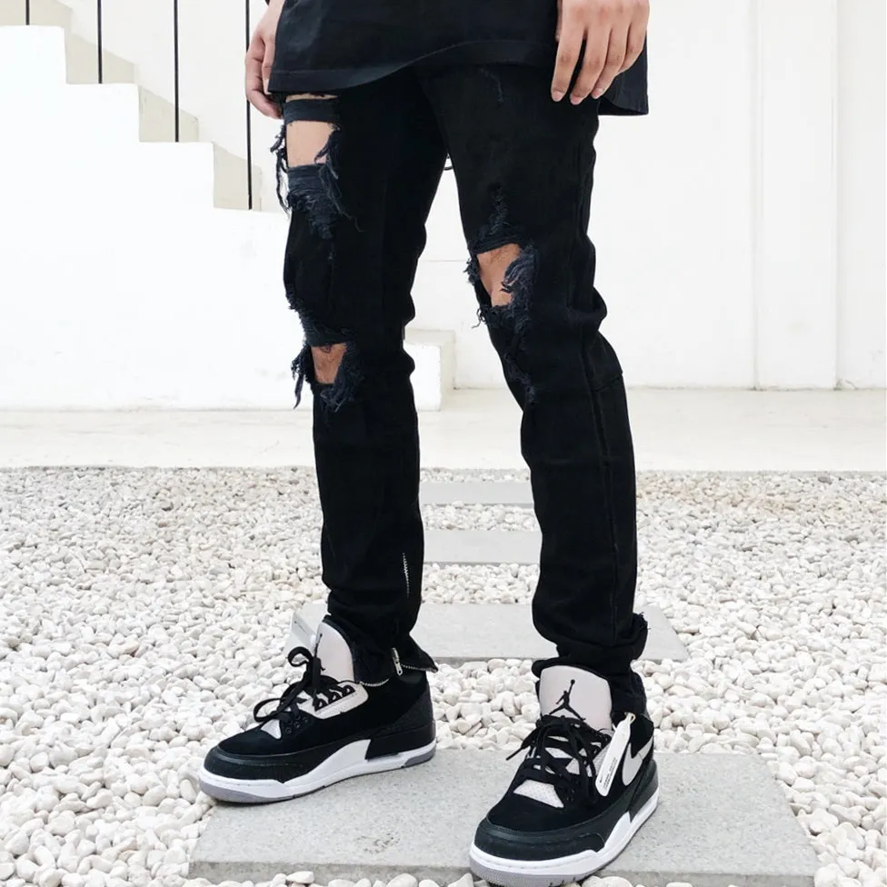 Men's high street style black torn jeans in washed black denim with raw edge details, front view.
