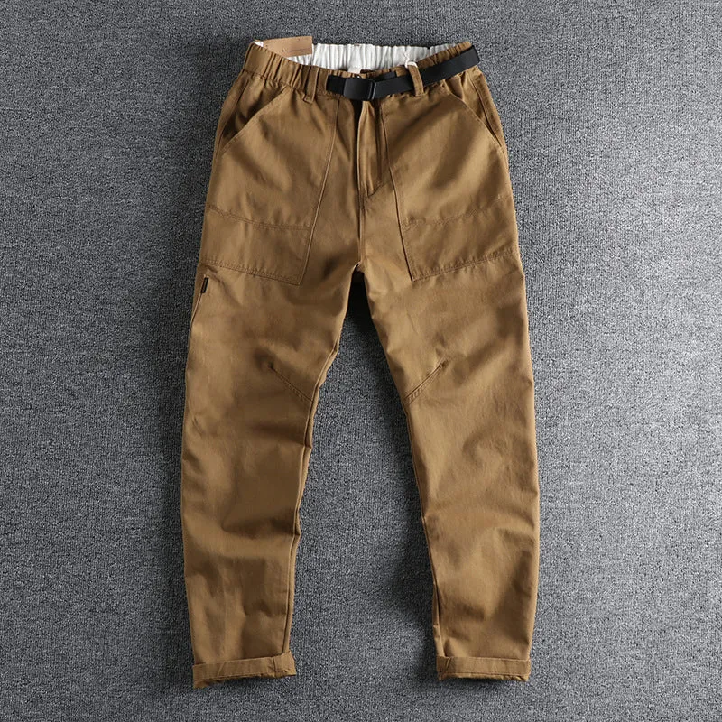Man wearing khaki cotton work trousers with a buckle belt and structured three-dimensional cut.
