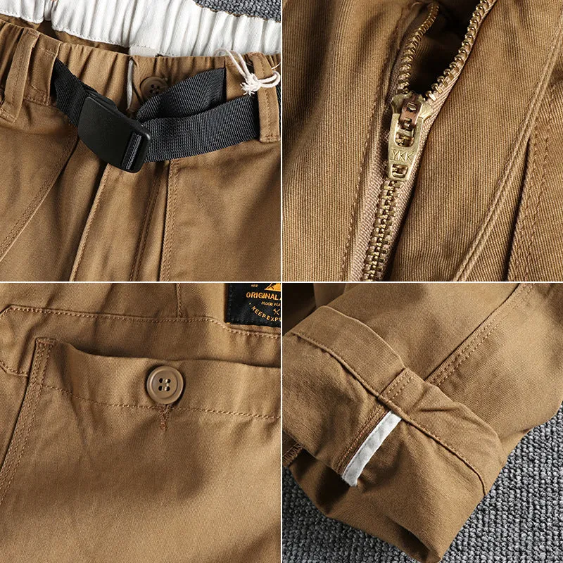 Man wearing khaki cotton work trousers with a buckle belt and structured three-dimensional cut.