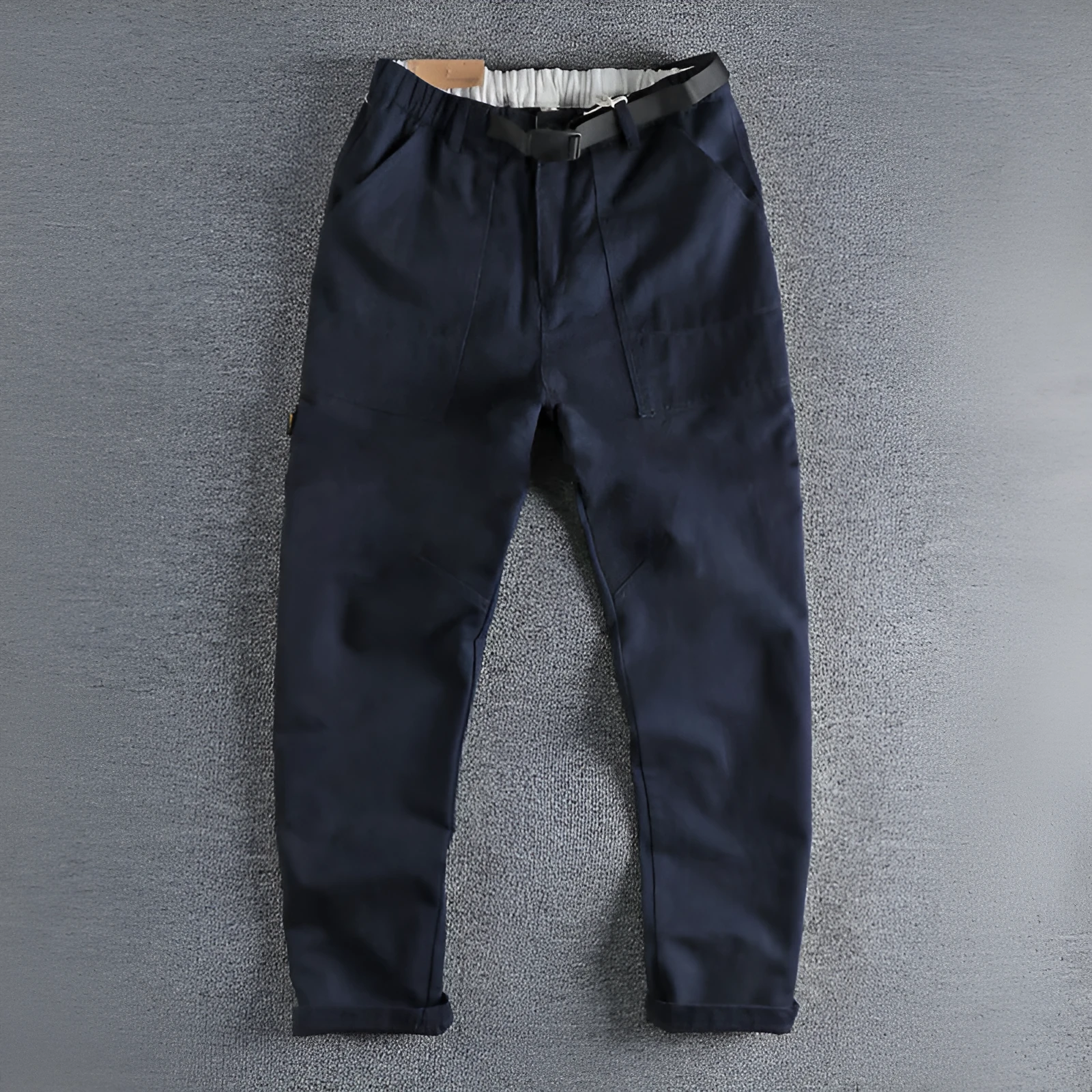 Man wearing khaki cotton work trousers with a buckle belt and structured three-dimensional cut.