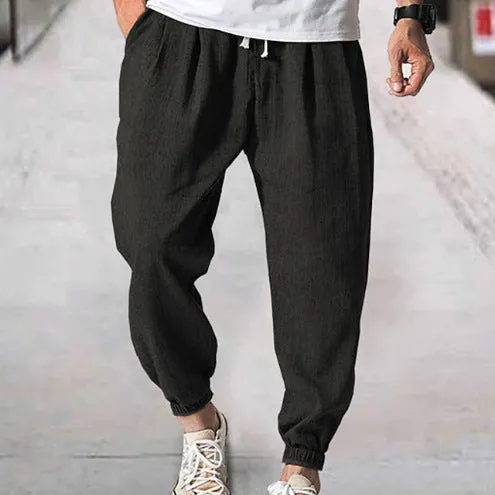 Man wearing loose light-coloured cotton trousers with elasticated ankle cuffs, showing front and side views.