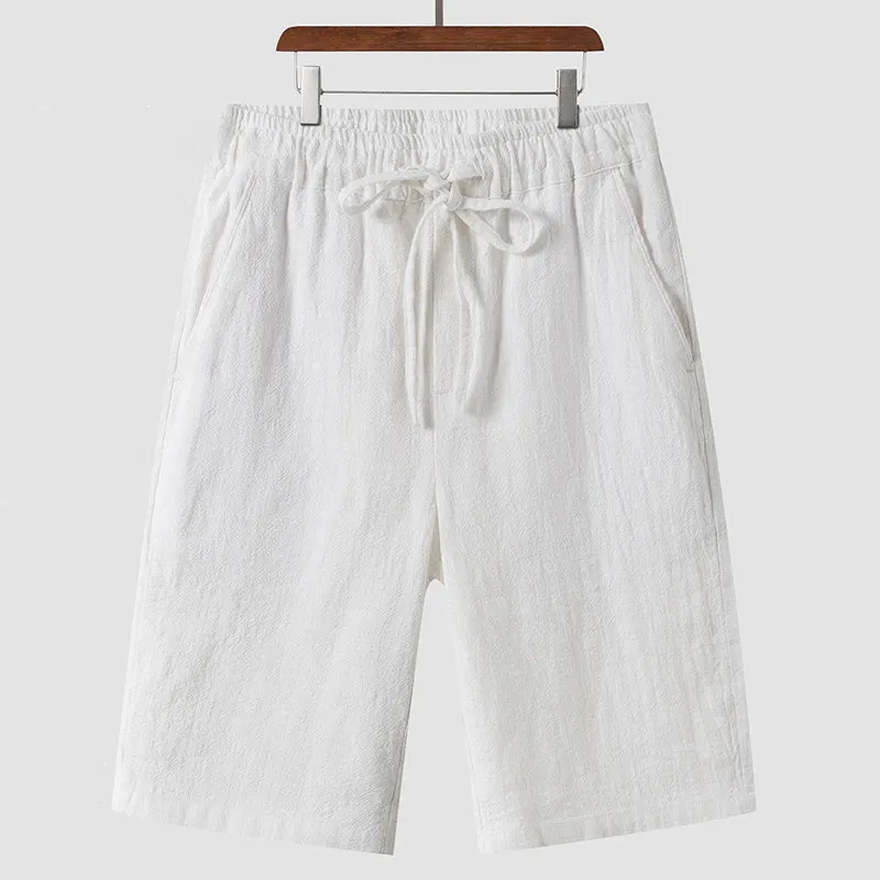 Pair of beige men's casual linen shorts with a loose fit and cropped length on a plain background.