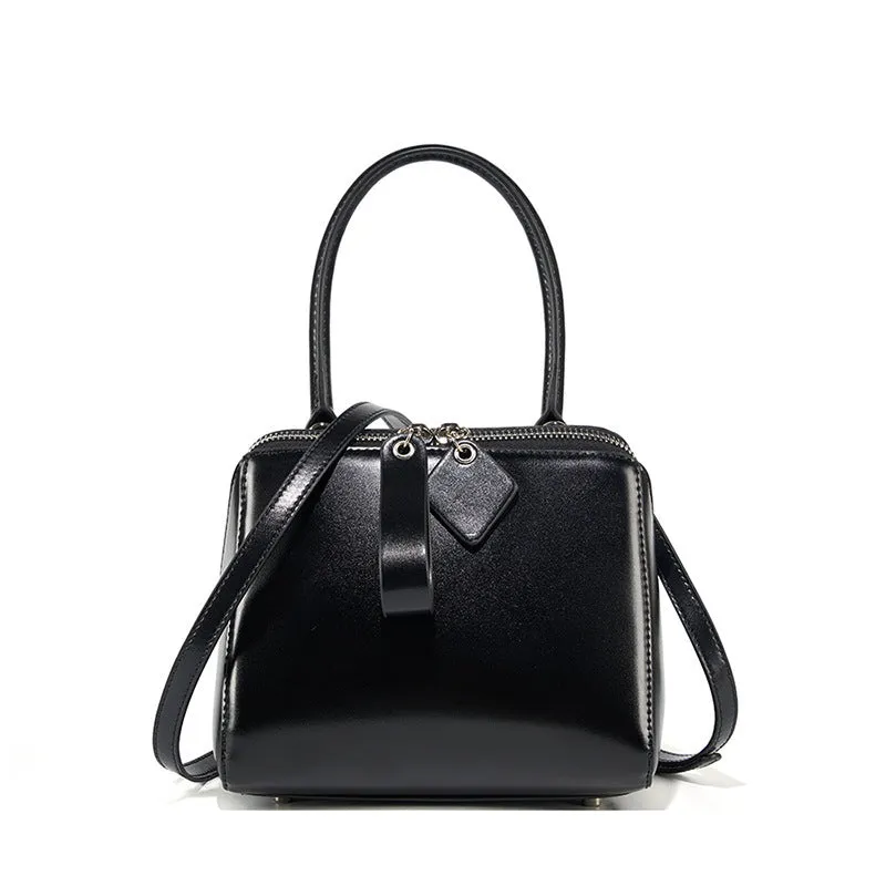 Open grain leather handbag in black with visible grain texture and welt pocket on front