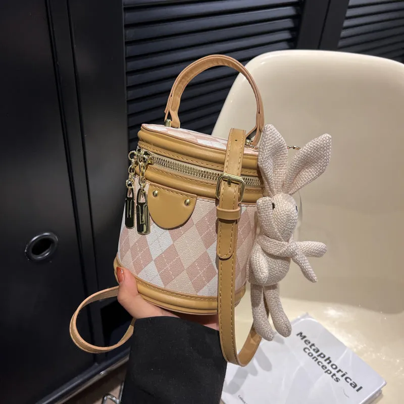 Textured rhombus cylindrical PU bucket bag in beige with white rabbit pendant, 14 cm wide.